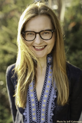 Portrait of Caucasian woman with blond hair and glasses wearing a blue shirt.